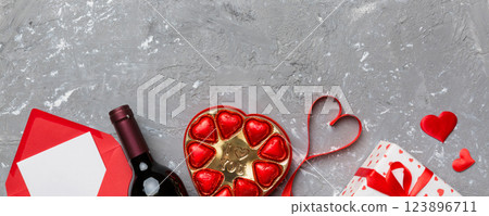 Bottle of red wine on colored background for Valentine Day with gift box, envelope and chocolate. Heart shaped with gift box of chocolates top view with copy space 123896711