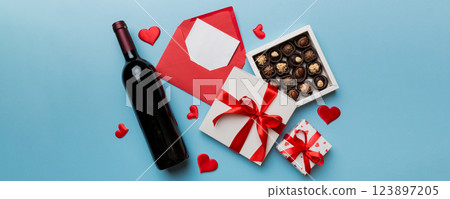 Bottle of red wine on colored background for Valentine Day with gift box, envelope and chocolate. Heart shaped with gift box of chocolates top view with copy space Bottle of red wine on colored background for Valentine Day with gift box, envelope and chocolate. Heart shaped with gift box of chocolates top view with copy space 123897205