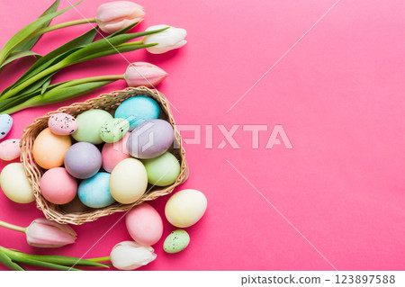 Happy Easter composition. Easter eggs in basket on colored table with yellow Tulips. Natural dyed colorful eggs background top view with copy space 123897588
