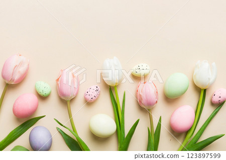 Happy Easter composition. Easter eggs on colored table with yellow Tulips. Natural dyed colorful eggs background top view with copy space 123897599