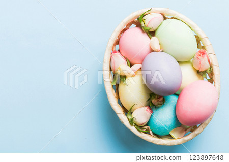 Happy Easter. Easter eggs in basket on colored table with yellow roses. Natural dyed colorful eggs background top view with copy space 123897648