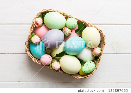 Happy Easter. Easter eggs in basket on colored table with yellow roses. Natural dyed colorful eggs background top view with copy space 123897663