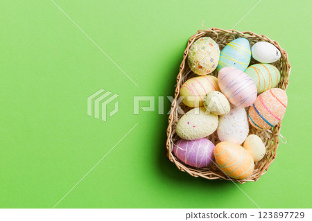 Colorful Easter eggs in wicker basket against colored background, closeup. top view with copy space 123897729