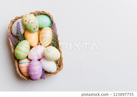 Colorful Easter eggs in wicker basket against colored background, closeup. top view with copy space 123897735