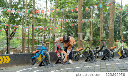 Young boy checking balance bike on outdoor course with flag decorations Young boy checking balance bike on outdoor course with flag decorations 123899958