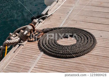 Coiled black rope on wooden dock near water with rusty metal cleats 123900428