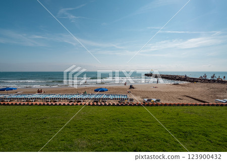 Relaxing beachfront with sunbeds and umbrellas along the sandy shore in Sitges, Spain Relaxing beachfront with sunbeds and umbrellas along the sandy shore in Sitges, Spain 123900432
