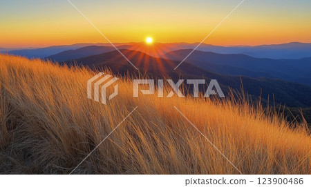 Golden sunrise illuminates mountain landscape with dry grass field 123900486