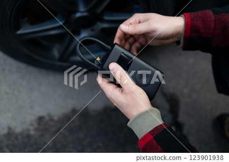 Close up of man hand holds a wireless portable air pump for inflating car tires. Self service, maintenance and safety.  123901938