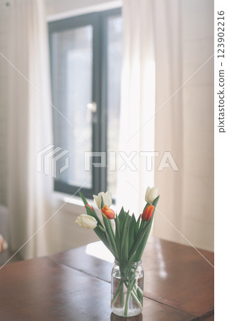 Bouquet of beautiful fresh tulips in a glass vase on wooden table in cozy modern interior. Spring flowers in glass vase at home. Bouquet of beautiful fresh tulips in a glass vase on wooden table in cozy modern interior. Spring flowers in glass vase at home. 123902216