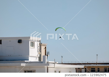 Paraglider mid-flight against clear blue sky in city 123902475