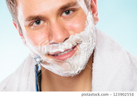 Young man shaving using razor with cream foam. 123902558
