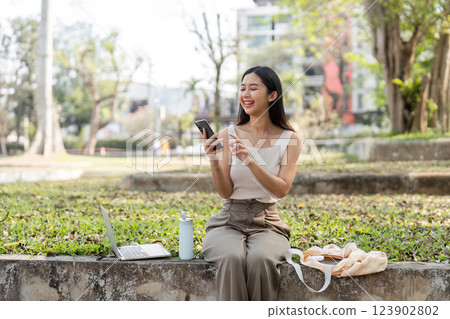Sustainable lifestyle. Cheerful young woman smiling while using her smartphone outdoors. Sustainable lifestyle. Cheerful young woman smiling while using her smartphone outdoors. 123902802