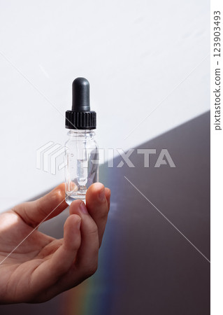 A close-up of a male hand with a transparent bottle of moisturizing serum for the face. A young man holds a cosmetic product in bright sunlight. A close-up of a male hand with a transparent bottle of moisturizing serum for the face. A young man holds a cosmetic product in bright sunlight. 123903493