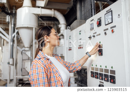 A young woman works at an elevator. An attractive female agronomist adjusts the machinery. The grain processing technician checks the equipment. 123903515