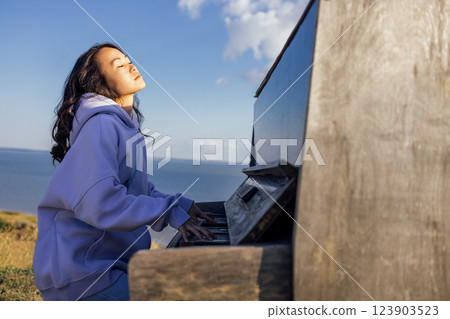 An attractive Asian woman has closed her eyes and is playing the piano outdoors. 123903523