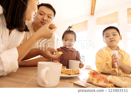 A happy Asian family is eating pizza in the kitchen at home. A young Korean couple and their cute children are having lunch. 123903531