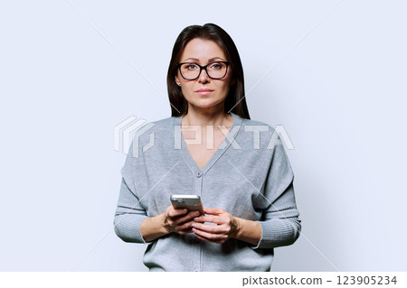 Middle aged beautiful woman holding smartphone looking at camera on white background Middle aged beautiful woman holding smartphone looking at camera on white background 123905234