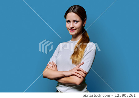 Beautiful young girl with crossed arms looking at camera on blue background 123905261