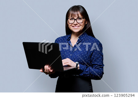 Portrait of middle aged businesswoman holding laptop on grey background 123905294