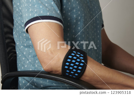 wears an epicondylitis bracelet sitting at his desk 123905318