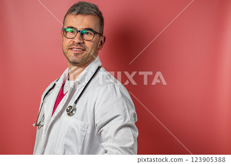 Professional doctor poses confidently with stethoscope against red backdrop Professional doctor poses confidently with stethoscope against red backdrop 123905388