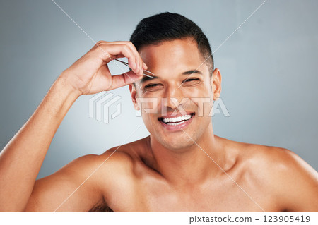 Portrait of a man tweezing his eyebrow with a tweezer in studio with gray background. Happy, smile and young guy plucking brow for hair removal for grooming, cleaning and hygiene routine or self care Portrait of a man tweezing his eyebrow with a tweezer in studio with gray background. Happy, smile and young guy plucking brow for hair removal for grooming, cleaning and hygiene routine or self care 123905419