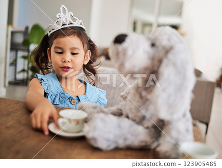 Girl, toy and tea party at a table with a princess crown, playing, having fun and talking in her home. Fantasy, creative and girl looking happy while talking to a teddy bear and drinking tea together 123905485