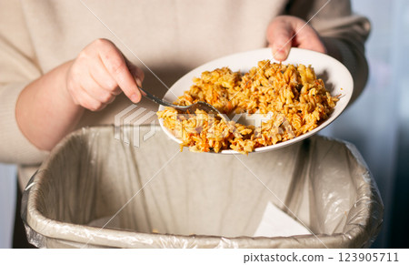 Woman holding food plate and throwing away food leftovers using spoon into garbage bin trash. Compost from leftover food. Stop Food Waste Day 123905711