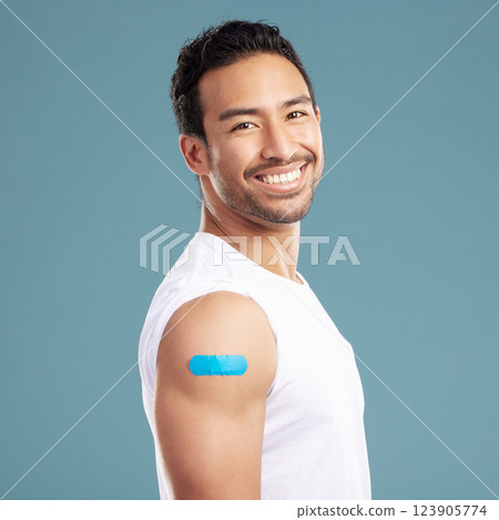 Studio, happy man and portrait with plaster for medicine, injection wound and safety for Influenza. Blue background, male person and smile with bandage for healthcare, vaccine and treatment for virus 123905774