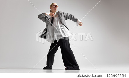 Low angle photo of young woman, dressed stylish oversized formal attire and dancing shows freedom and individuality, against white studio background. 123906364