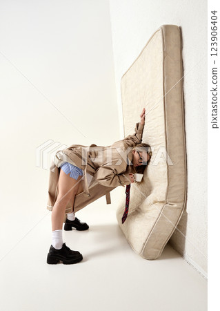 Young woman, employee, posing bending forward, hand on mattress, sipping coffee with drained expression. Burnout. 123906404