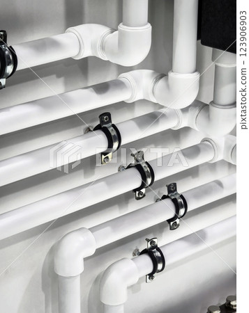 Detailed view of white plumbing pipes installed on a wall in a modern building environment Detailed view of white plumbing pipes installed on a wall in a modern building environment 123906903