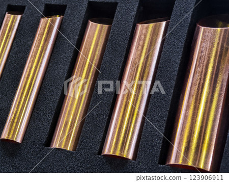 Metallic copper tubes arranged carefully in a black foam holder, displaying smooth surfaces and reflective qualities in a workshop setting 123906911