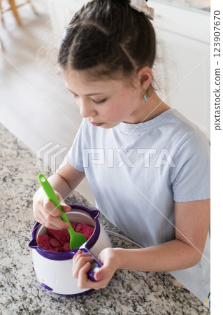 With focused attention, this budding culinary artist dips pretzels into a pot of melted chocolate, creating sweet delights in the warmth of a well-lit home kitchen. 123907670