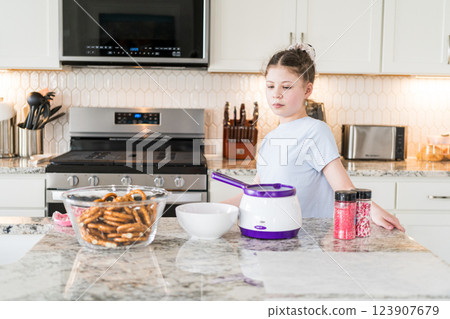 With focused attention, this budding culinary artist dips pretzels into a pot of melted chocolate, creating sweet delights in the warmth of a well-lit home kitchen. 123907679