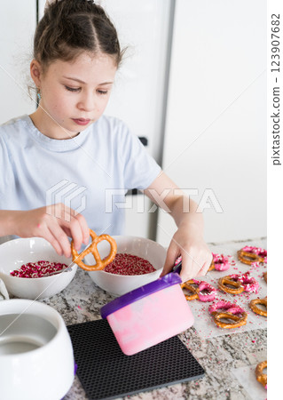 With focused attention, this budding culinary artist dips pretzels into a pot of melted chocolate, creating sweet delights in the warmth of a well-lit home kitchen. With focused attention, this budding culinary artist dips pretzels into a pot of melted chocolate, creating sweet delights in the warmth of a well-lit home kitchen. 123907682