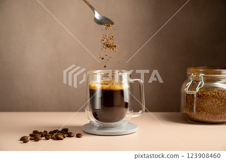 Instant coffee pouring in transparent glass mug, roasted coffee beans 123908460