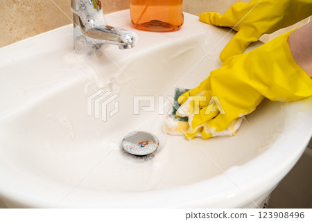 Cleaning bathroom basin and water tap, yellow gloves and spray detergent Cleaning bathroom basin and water tap, yellow gloves and spray detergent 123908496