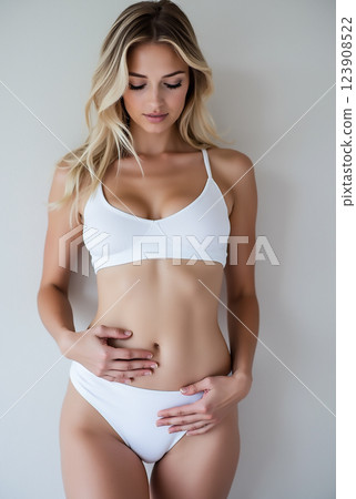 Young woman in a white bikini standing against a neutral background, exuding confidence and grace in a serene atmosphere 123908522