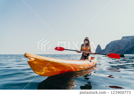 Kayaking Woman Sea - A woman kayaks on the calm waters of the sea with a mountain in the background. 123908773