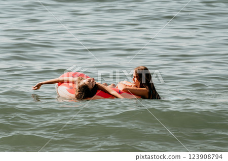 Two Young Women Relaxing on a Donut Float in the Ocean Two Young Women Relaxing on a Donut Float in the Ocean 123908794