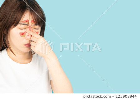 Asian woman suffering from sinusitis with nasal congestion of mucus or pus over blue background. Causes of rhinosinusitis include bacterial infections, viral infections and allergies. 123908944
