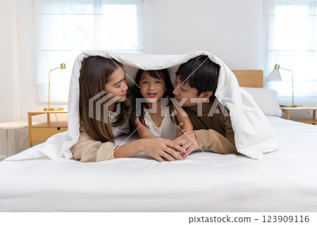 Happy father mother daughter lie down and play on bed. Mom dad and little girl smiling cheerful bedroom. relaxing in holiday. Happy father mother daughter lie down and play on bed. Mom dad and little girl smiling cheerful bedroom. relaxing in holiday. 123909116