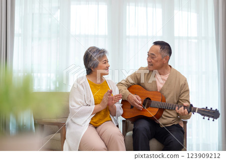 Happy asian senior elderly couple take it easy on retirement holidays playing guitar having fun in living room at home, Happiness singing together. Taking care of each other health in old age. 123909212