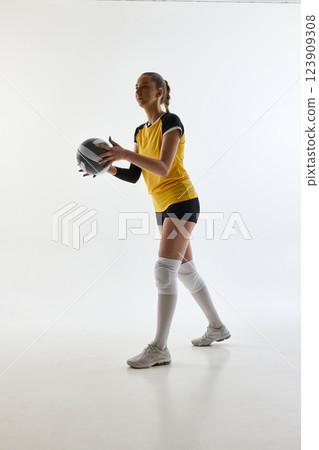 Full-length image of young woman, volleyball player in uniform, standing with determination, serving ball, playing 123909308