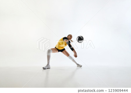 Energetic action shot of female volleyball player in yellow jersey, hitting ball with precision, isolated on white background. Energetic action shot of female volleyball player in yellow jersey, hitting ball with precision, isolated on white background. 123909444