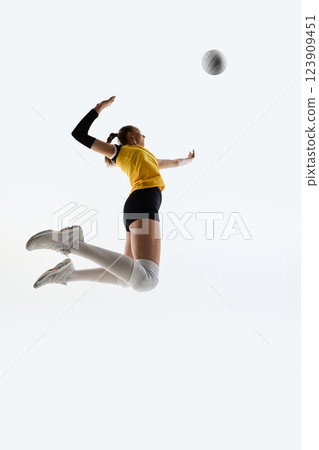 Low angle view of young athlete hitting volleyball, showing energy of game, training against white studio background. 123909451