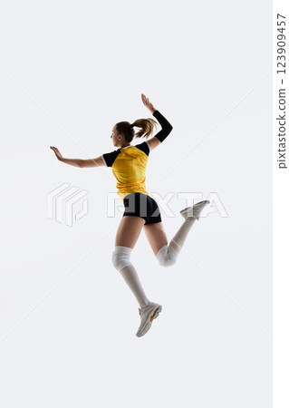 Full-length of young woman, volleyball player n yellow jersey and black shorts jumping, training isolated on white background. 123909457