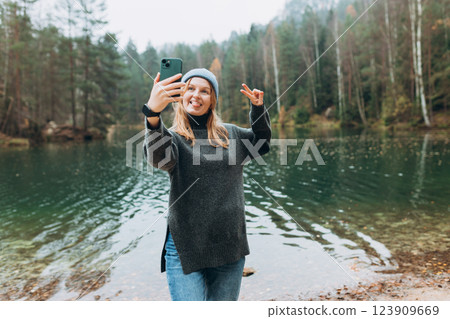 Happy blonde Woman makes selfie mobile photo enjoying mountain lake landscape. Nature freedom adventure, vacation video call, girl tourist outdoors. Concept of an active lifestyle 123909669